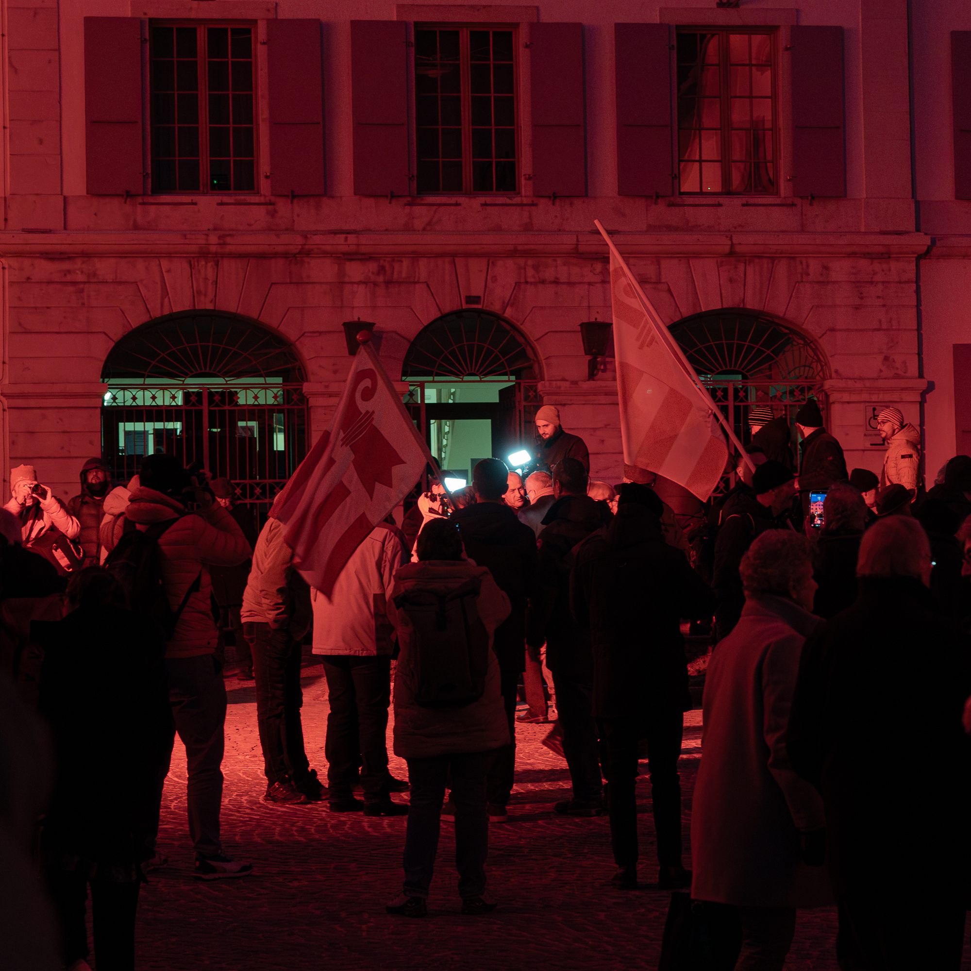 Foule et drapeaux jurassiens devant l’hôtel de ville de Moutier, éclairés en rouge