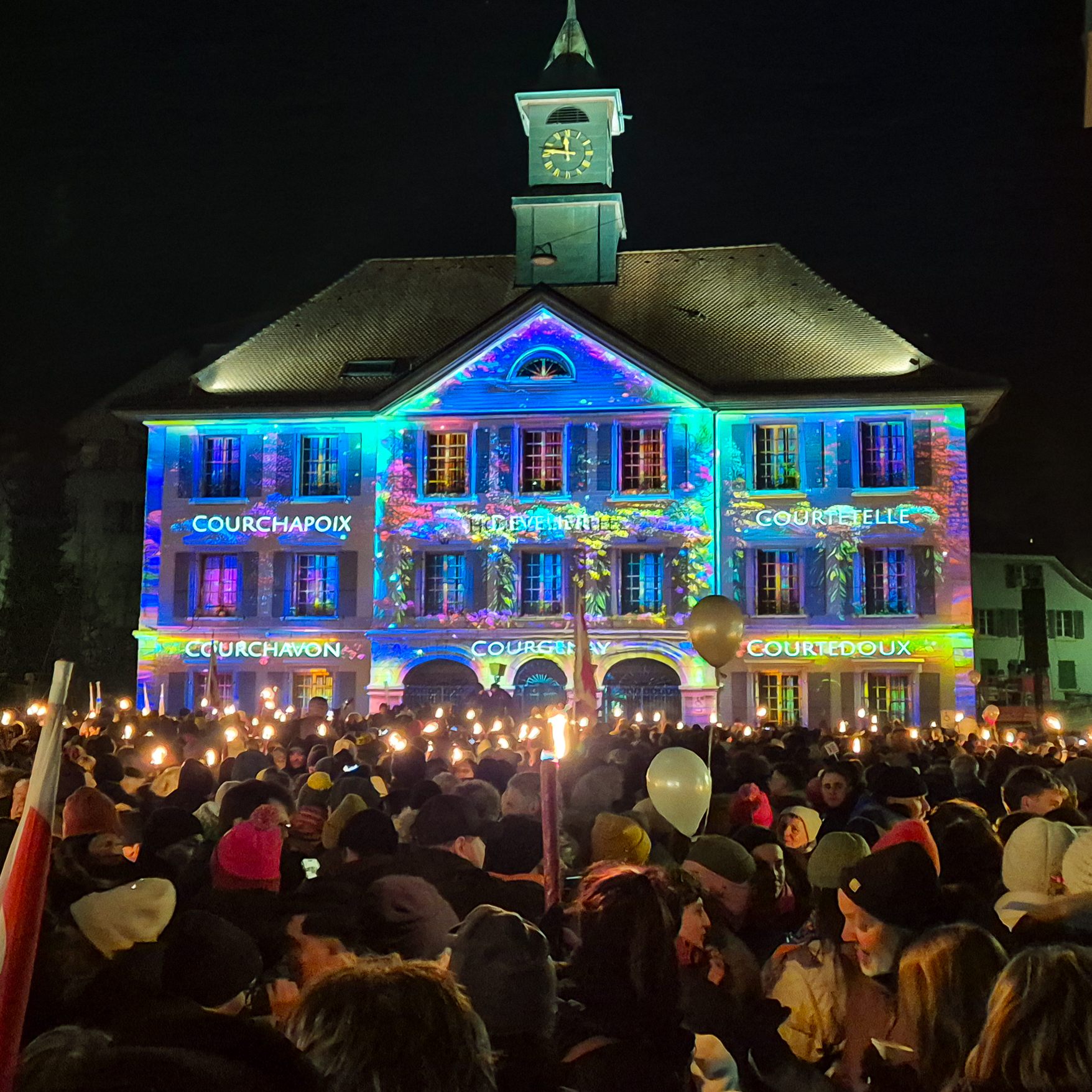 Projection lumineuse sur l’hôtel de ville de Moutier devant une foule aux flambeaux